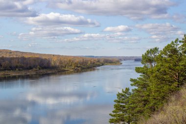 Ormanların arasında güzel, geniş bir nehir sonbaharı. Sonbahar renkleriyle sakin ve sessiz bir yer. Bulutların ve ormanların güzel havalarda suda yansıması.