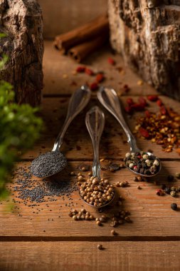 Ahşap bir masada baharatlı üç gümüş kaşık, kuru kırmızı biber, kişniş ve haşhaş tohumu.