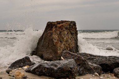 Yunanistan 'da bulutlu bir gökyüzünde dalgaların vurduğu denizdeki karanlık kayalar