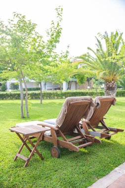 Yazın ağaçların altındaki bahçede şilteli tahta güneşlikler.