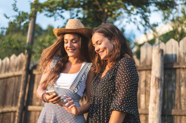 Akıllı Telefon Kullanan ve Gülümseyen İki Güzel Kız Arkadaş. Çiftlik Konsepti Fotoğrafçılık