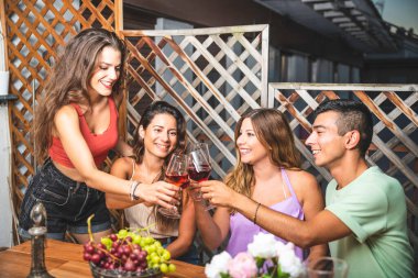 Mutlu arkadaşlar yüksek sesle gülüyor ve kırmızı şaraba kadeh kaldırıyor. Masada beyaz ve kırmızı üzümlerle birlikte. Arkadaşlarla Balkon Konsepti Eğlenerek Zaman Geçiriyorlar.