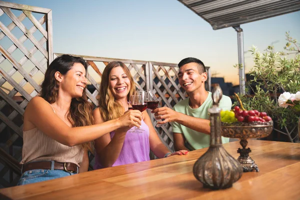 Three Friends Laughing and Cheering With Glasses of Wine at The Balcony. People Sitting at the Balcony