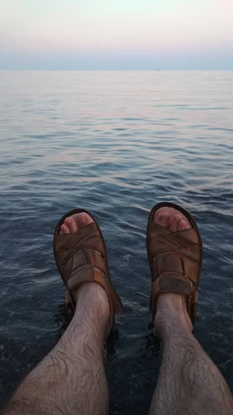 Male feet in sandals on the rock. Rest on the seashore, summer vacation.