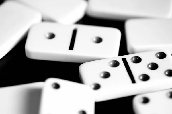 Dominoes are scattered on a dark surface close up. Black and white