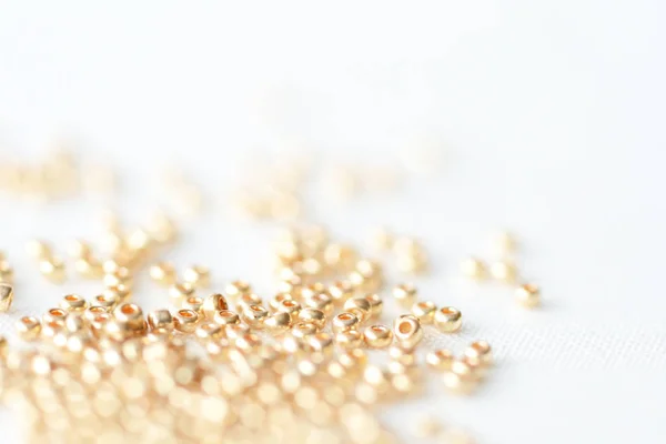 Golden seed beads scattered on textile background close up