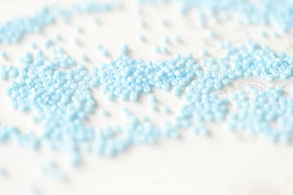 Seed beads light blue color scattered on a textile background close up