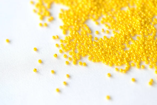 Seed beads yellow color scattered on a textile background close up