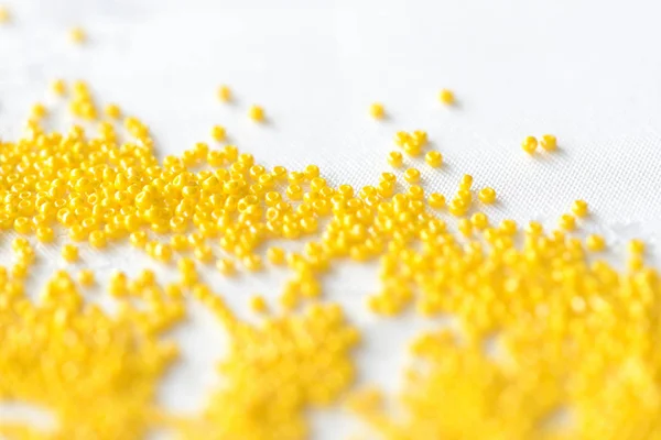 Seed beads yellow color scattered on a textile background close up