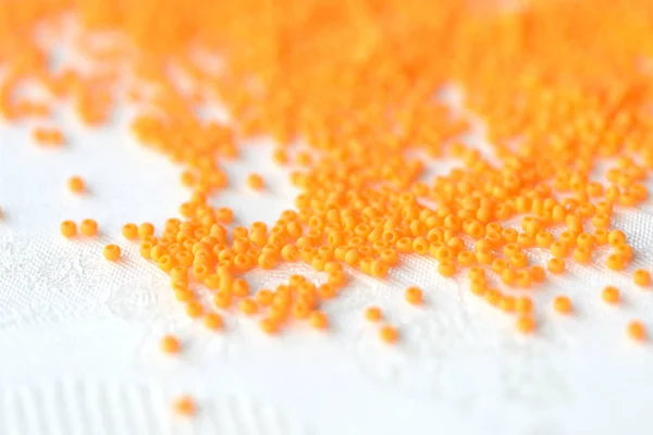 Opaque seed beads orange color scattered on a textile background close up