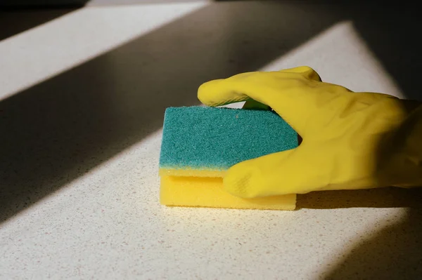 Hand in yellow rubber glove washing surface on a sunny day. Spring cleaning	brown color toned