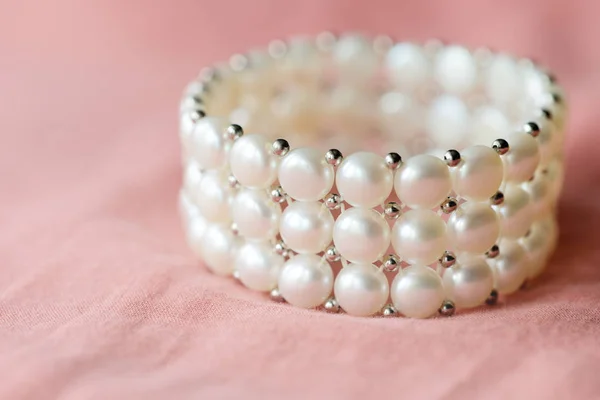 Beautiful white pearl bracelet on a coral textile background close up