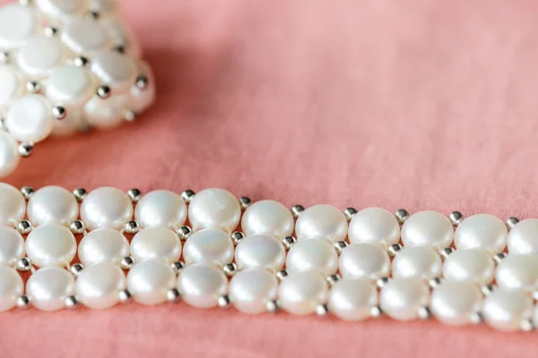 Beautiful white pearl necklace on a coral color textile background close up