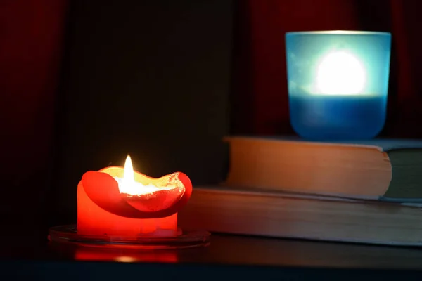 Red burning candle and old books in the dark close up