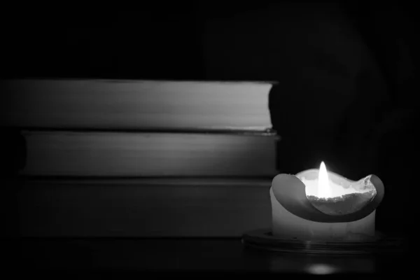 Burning candle and old books in the dark close up. Black and white