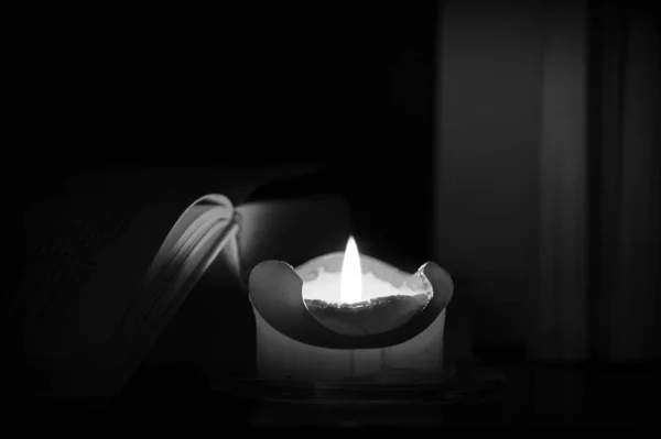 Burning candle and old books in the dark close up. Black and white