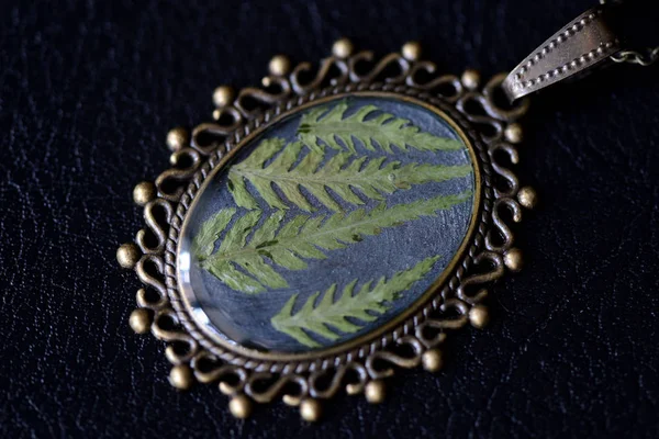 Pendant made of epoxy resin and fern leaf on a dark background close up