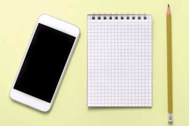 Boş not defteri, telefon ve kalem sarı bir arka plan üzerinde yakın