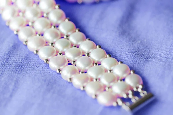 Fragment of a white pearl necklace on a purple color textile background close up