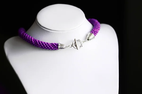 Purple necklace made of seed beads on a dark background close-up
