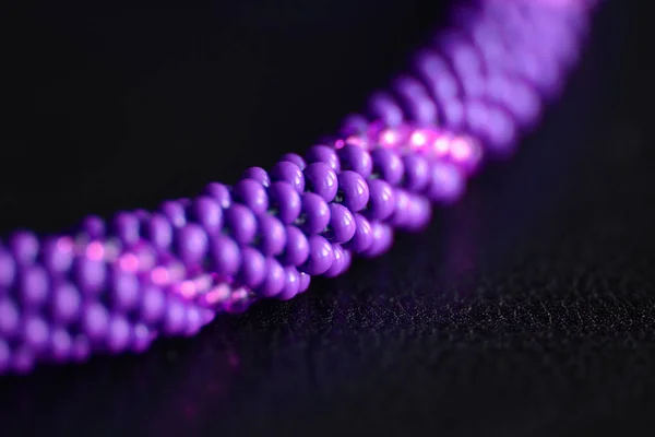 Purple necklace made of seed beads on a dark background close-up