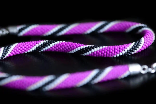 Beaded necklace purple, black and white colors on a dark background close up