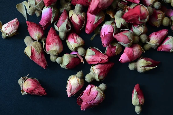 Dried rose buds scattered on a dark surface close up