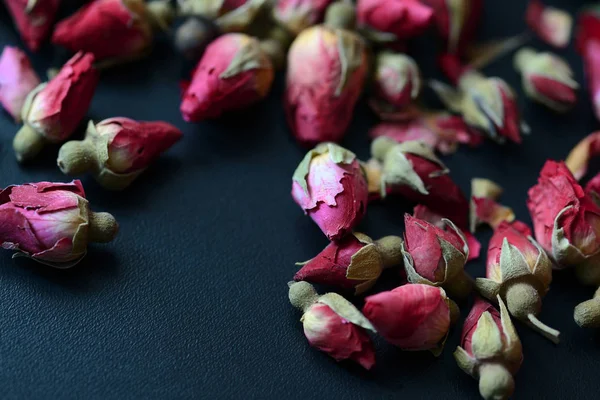 Dried rose buds scattered on a dark surface close up