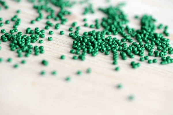 Scattered seed beads of emerald color on the wooden background