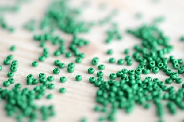Scattered seed beads of emerald color on the wooden background