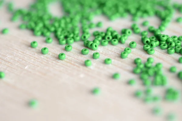Scattered seed beads of green color on the wooden background