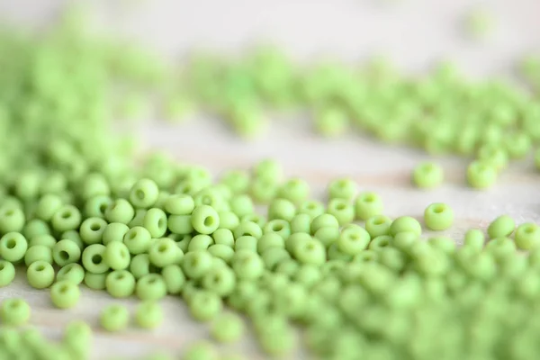 Seed beads of light green color scattered on a wooden surface close-up