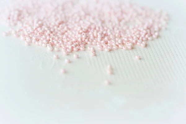 Pink seed beads scattered on the textile background close up. Handmade concept