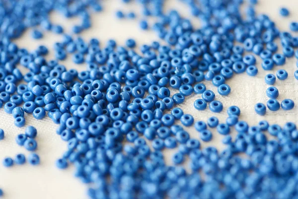 Seed beads blue color scattered on a textile background close-up. Handmade, art, creativity