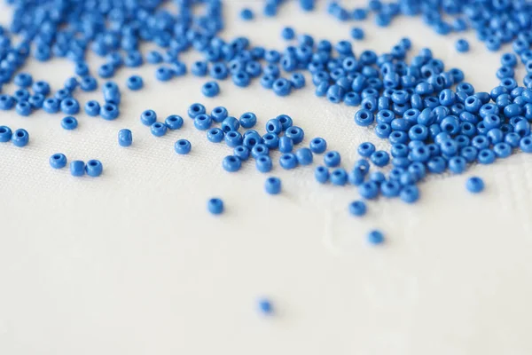 Blue seed beads scattered on a white textile background closeup. Handmade concept