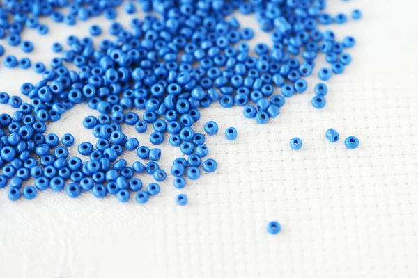 Blue seed beads scattered on a white textile background closeup. Handmade concept