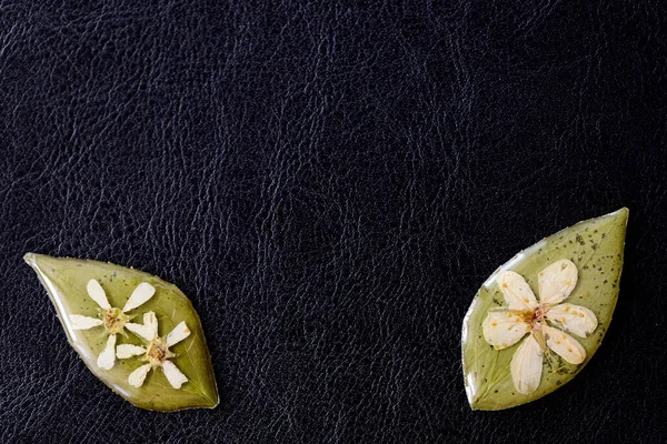 Flowers on a leaf drenched with epoxy resin on a dark background close-up. Top view, copy space. Elements for handmade jewelry made of resin and natural material