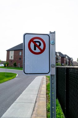 Siyah bir çit ve arka planda bir bina ile yolun kenarında bir park işareti