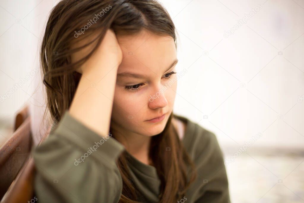 Unhappy depressed teenager with face in hands sitting on the bench