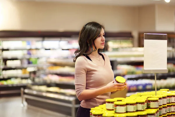 Woman choosing daily products at supermarket. Reading product information. Concept of conscious choice of healthy and quality food.