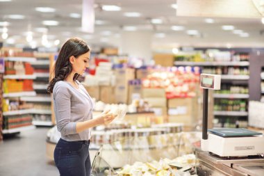 Kadın süpermarkette günlük ürünler seçiyor. Ürün bilgileri okunuyor