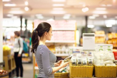 Kadın süpermarkette günlük ürünler seçiyor. Ürün bilgileri okunuyor