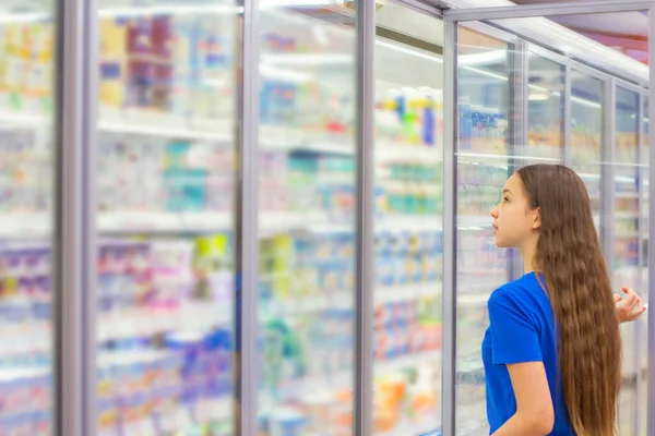 Teen girl shopping in supermarket, reading product information, choosing daily product. Concept of conscious choice of healthy food by teenager\'s.