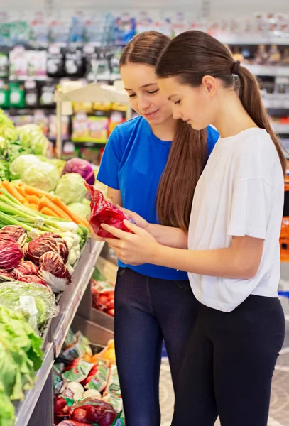 Teen girls shopping in supermarket, reading product information, choosing daily product. Concept of conscious choice of healthy food by teenager's.