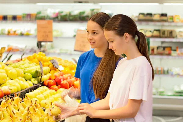 Genç kızlar süpermarkette alışveriş yapıyorlar, ürün bilgileri okuyorlar, günlük ürünleri seçiyorlar. Gençlere göre bilinçli sağlıklı yiyecek seçimi kavramı.