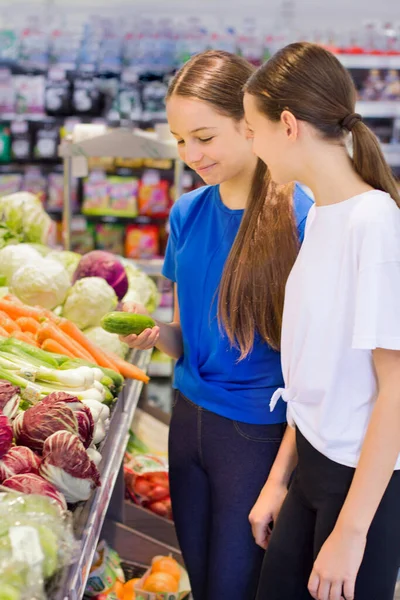 Teen girls shopping in supermarket, reading product information, choosing daily product. Concept of conscious choice of healthy food by teenager\'s.
