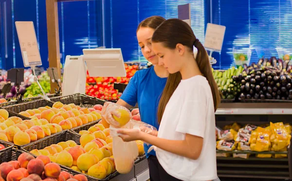 Genç kızlar süpermarkette alışveriş yapıyorlar, ürün bilgileri okuyorlar, günlük ürünleri seçiyorlar. Gençlere göre bilinçli sağlıklı yiyecek seçimi kavramı.