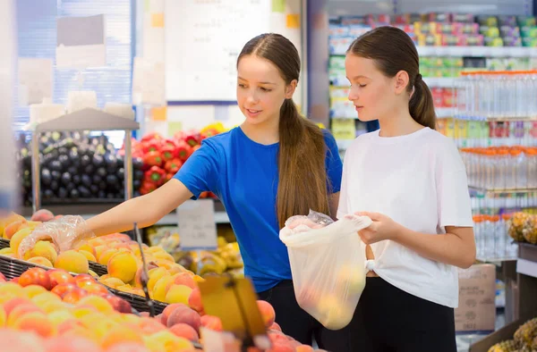 Genç kızlar süpermarkette alışveriş yapıyorlar, ürün bilgileri okuyorlar, günlük ürünleri seçiyorlar. Gençlere göre bilinçli sağlıklı yiyecek seçimi kavramı.