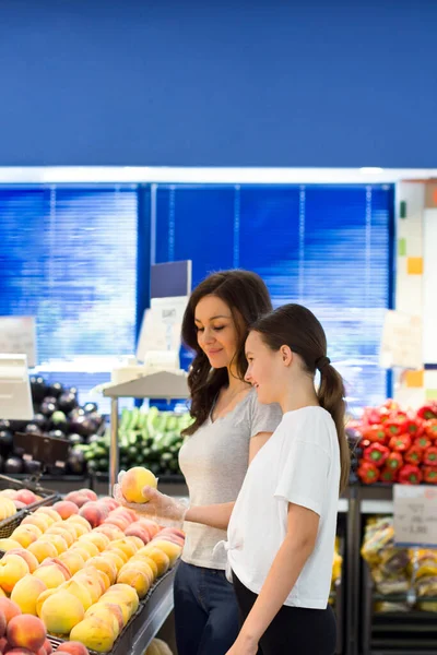 Teen girl with mother shopping in supermarket at  fruit section. Choosing daily product