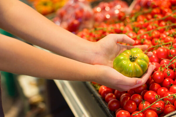 Female hand choosing tomato in supermarket. Concept of conscious choice of healthy food.